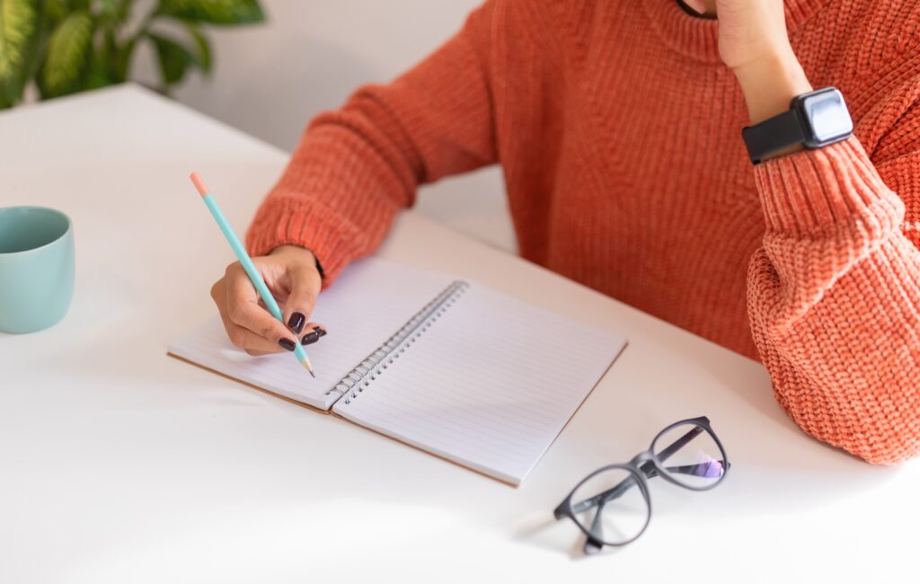 Professional woman in sweater writing notes on pad, wearing smartwatch, focused on productivity